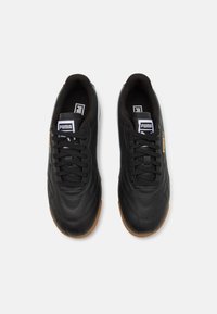 Črne usnjene superge z teksturirano površino, okroglo špico in črnimi vezalkami. Ponašajo se z gumijastim podplatom in belim logotipom na jeziku.