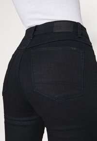 Mustat farkut, joissa on istuva malli, erottuvat takataskujen ompeleet ja teksturoitu vyötärönauha paremman pidon takaamiseksi.