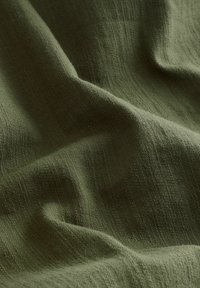 Tissu vert olive, texturé avec une finition douce et mate, affichant de doux plis et creases, mettant en évidence sa légèreté et sa respirabilité.