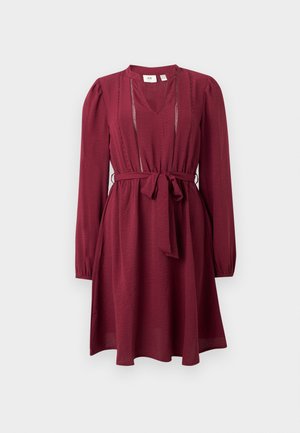 Abito bordeaux con maniche lunghe, scollo a V, vita cinchata e cintura legata; presenta una delicata cucitura lungo il collo. Texture del tessuto liscia.