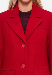 Red wool-blend blazer with notched lapels, three buttons, and a left chest pocket, textured fabric, and tailored fit.