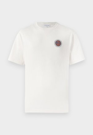 T-shirt bianco in cotone a maniche corte, con un logo circolare blu e arancione "Tennis Heritage" sul lato sinistro del petto.