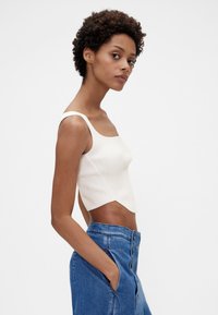 Ribbede strikkede cropped top i off-white, med brede stropper og en bølget kant. Kombineret med blåt denimnederdel med høj talje.
