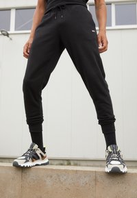 Svarta träningsoveraller med elastiska muddar och dragsko i midjan, i kombination med flerfärgade sneakers med nät- och gummidesign.