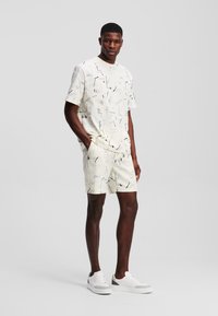 Lyst farvet kortærmet skjorte og shorts sæt med abstrakte sorte og blå mønstre, parret med hvide sneakers. 100% bomuldsstof.
