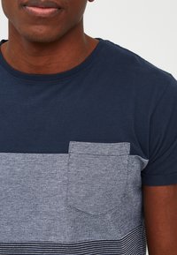 Navy blue t-shirt with a light blue striped pattern, featuring a chest pocket and short sleeves, made from cotton blend fabric.