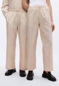 Ριγέ παντελόνι σε ανοιχτό ροδακινί απόχρωση με ελαστική μέση και κορδόνι. Ομαλό ύφασμα με κάθετες γραμμές σε σκουρές και ανοιχτές αποχρώσεις. Συνδυάζεται με μαύρα παπούτσια.