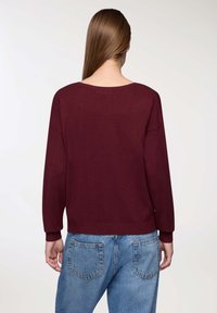Pullover in magenta a maglia con scollo ampio e maniche lunghe, abbinato a jeans in denim leggero a vita alta di colore blu con tasche posteriori.