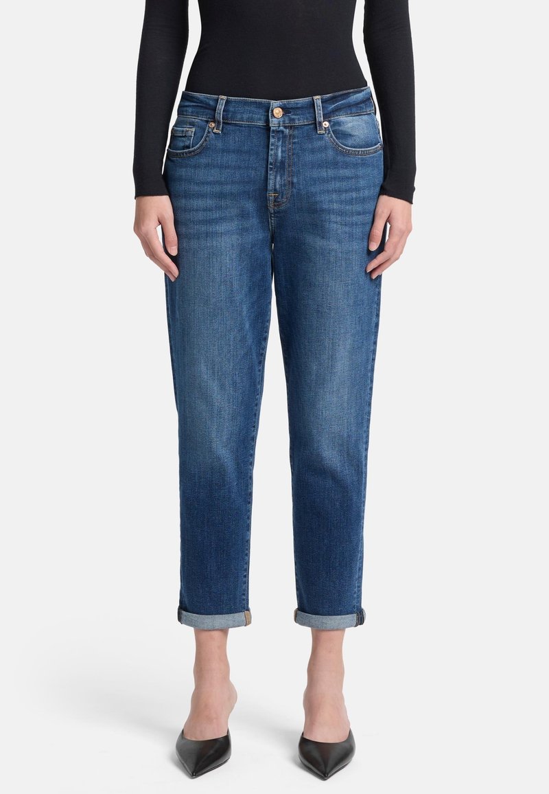 Jeans in denim blu scuro con taglio dritto, orli arrotolati, cinque tasche e dettagli in bottone bronzato, abbinati a un top attillato a maniche lunghe.