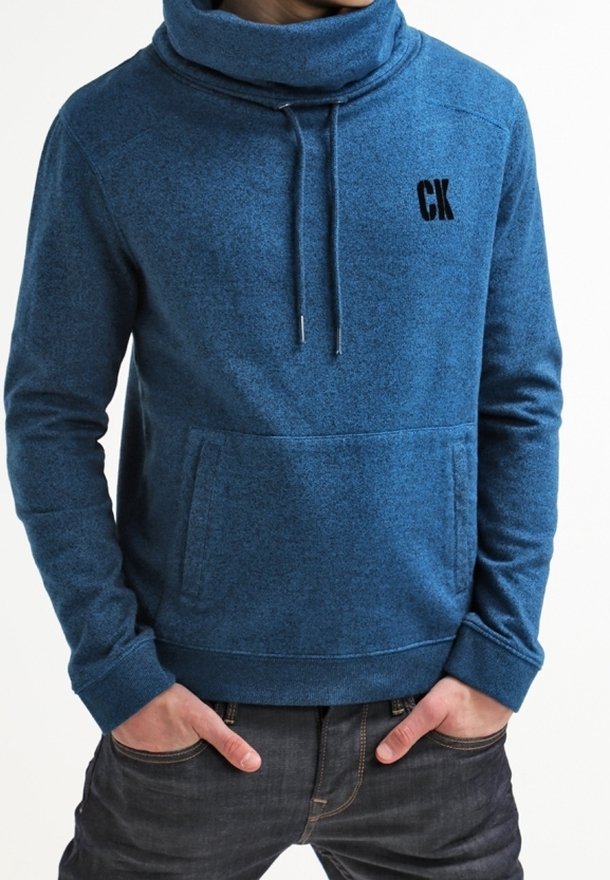 Sudadera azul de textura, de manga larga, con cuello alto y cordones. Cuenta con un bolsillo canguro en la parte frontal y el logo bordado "CK" en la tela.