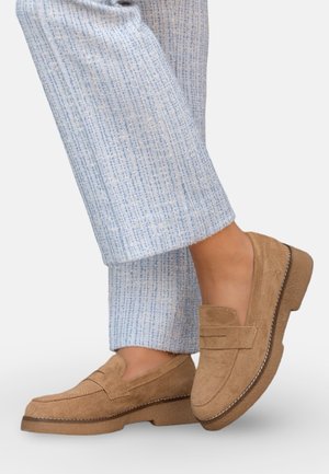 Pantalon texturé bleu clair associé à des mocassins en suède beige avec une semelle épaisse et des coutures apparentes.