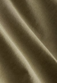 Gros plan sur un tissu beige avec une texture visible et des plis doux créant de légères ombres et des reflets.
