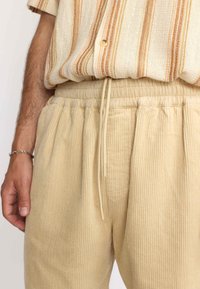 Beige corduroy broek met een gestructureerd verticale ribpatroon, voorzien van een elastische tailleband en een trekkoord voor een verstelbare pasvorm.