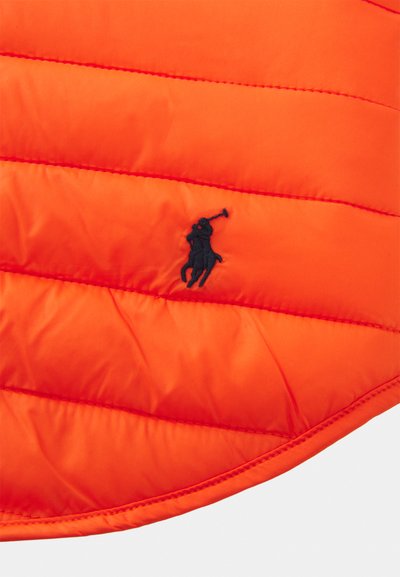 Padded orange Jacke mit horizontalen Nähten, glatter Textur und einem schwarzen gestickten Logo eines Pferdereiters mit einem Schläger.