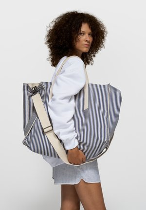 Bolso tote de lona a rayas en azul y blanco, con un diseño espacioso, correa de hombro ajustable y cierre superior con cremallera.