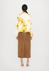 Floral-patterned, white long-sleeve jacket with yellow flowers; brown, mid-length skirt; beige ankle-strap heels; smooth textures.