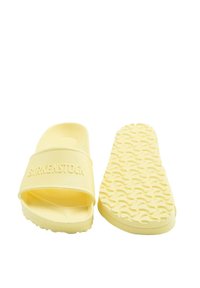 Chanclas de goma amarillas con una tira texturizada y el logotipo de "Birkenstock", además de una suela con un diseño que proporciona tracción.