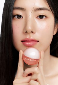Boîte transparente de masque pour les lèvres avec une base rose et un couvercle blanc, tenue entre les doigts. Texture lisse, étiquetée "Abib PDRN collagen lip mask".