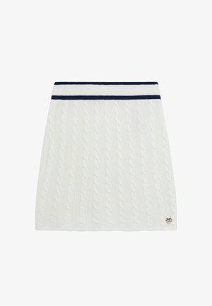 Jupe en maille torsadée blanche avec une ceinture à double bande bleu marine et un petit emblème doré au bas côté droit.