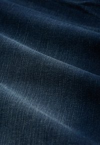 Tissu en denim de teinte bleu foncé, présentant une texture lisse avec des variations de couleur subtiles et de légers motifs de tissage diagonal.