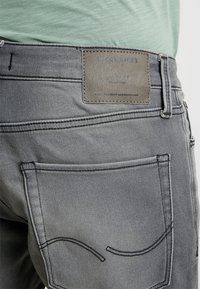 Vaqueros de mezclilla gris con un diseño clásico de cinco bolsillos, costuras decorativas en los bolsillos traseros y un parche de cuero texturizado de la marca.