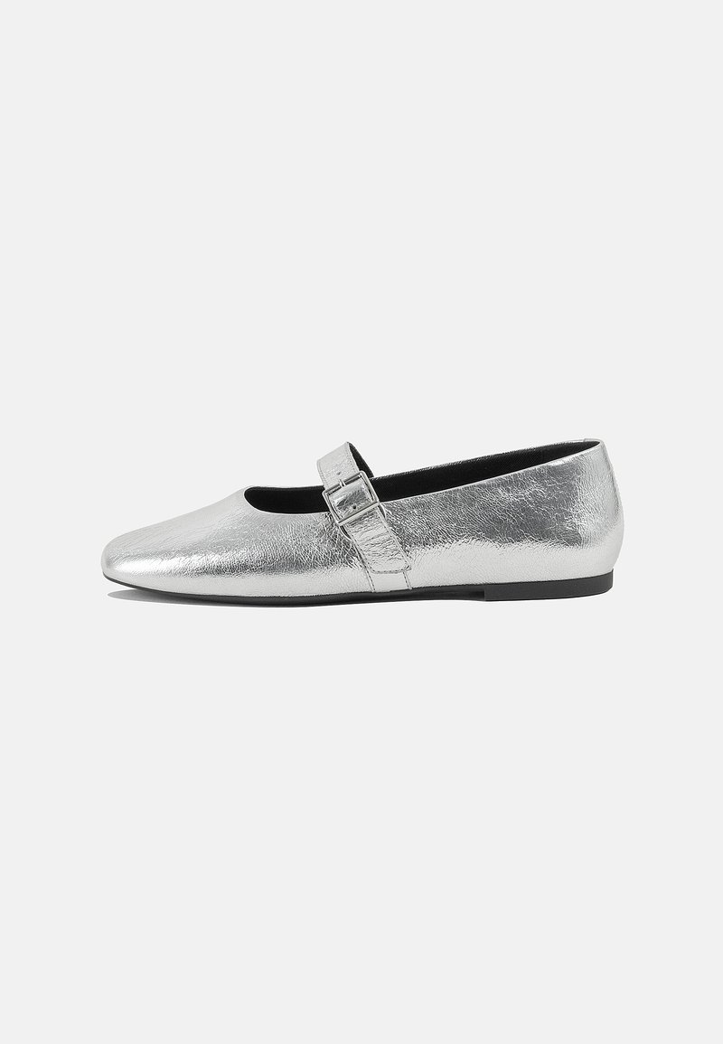 Ballerine metallizzate argento con punta affilata e chiusura con fibbia laterale. Texture liscia, tacco nero basso, design minimalista.