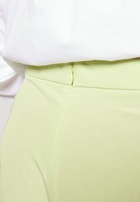 Calças verde claro com um fecho oculto na cintura. Textura suave com um corte entalhado e detalhes de costura discretos.