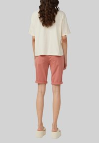 Korte crèmekleurige t-shirt, roze opgerolde shorts en witte platformsandalen; gladde stof en een ontspannen pasvorm met achterzakken op de shorts.