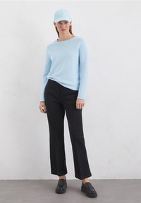 Helles blaues langärmliges Strickpullover, schwarze weite Hosen und eine hellblaue Mütze. Schwarze Slipper runden das Outfit ab. Glatte Texturen durchgängig.