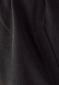 Crni teksturirani materijal s mekanim naborima, s bočnom džepom i elegantnim, minimalističkim dizajnom.