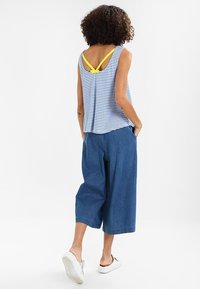 Gestreept tanktop met gele accenten, gecombineerd met brede blauwe denim culottes. Beschikt over een relaxed fit en subtiele textuur. Witte sneakers maken de look compleet.