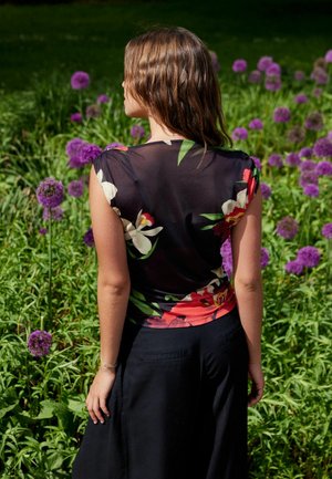 Ung kvinna med blöt brunt hår, iförd en blommig topp och svart kjol, står med ryggen mot kameran i ett fält av lila blommor.