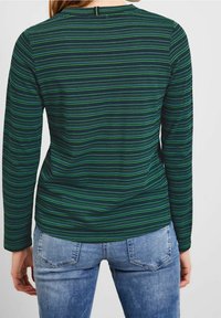 Grön och marinblå randig långärmad topp med ett strukturerat mönster, rundad halsringning och en liten öppning i ryggen. Matchad med ljusblå jeans.