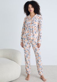 Blumenmuster Pyjama-Set mit einem Hemd mit Knöpfen und passenden Hosen. Das Material ist weich, mit Pfirsich- und blauen Blumen auf einem hellen Hintergrund.