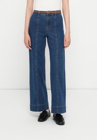 Široke modre denim hlače z kontrastnim šivanjem, visokim pasom in pletenim rjavim pasom. Imajo ravno prileganje in strgan rob.