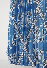 Sininen laskostettu kangas, jossa on valkoisia ja mustia paisley- ja kukkakuvioita, jotka muodostavat geometrisia muotoja.