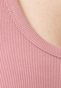 Prašno růžový žebrovaný tank top, který má široký výstřih a texturovanou látku. Švy podél okraje jsou úhledné a konzistentní.