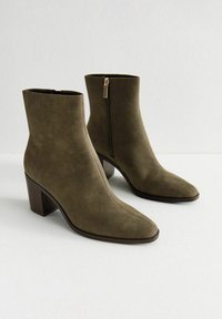 Bottines vert olive en suède doux, avec un bout pointu et un talon épais, une fermeture éclair sur le côté et une texture lisse.