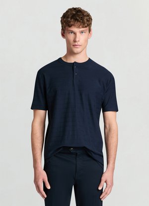 Marineblaues Henley-Shirt mit kurzen Ärmeln und drei Knöpfen, mit einem strukturierten Streifendesign. Kombiniert mit dunkler Hose.