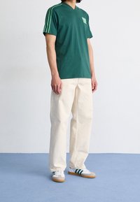 Green v-neck t-shirt with green stripes on sleeves, paired with off-white wide-leg pants and white sneakers with green accents and gum soles.