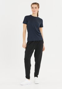 Marinblå t-shirt med kort ärm, parat med svarta smala byxor; modellen bär vita sneakers. Slät tyg, avslappnad passform, minimal varumärkesprofil.