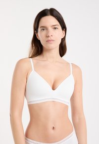 White bralette with a deep V-neck, adjustable straps, and lace trim along the bottom. Smooth fabric with a minimalist design.