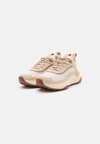 Baskets de sport beige clair avec une tige en mesh texturé, semelle en caoutchouc et accents roses discrets sur la languette et les lacets. Design arrondi.
