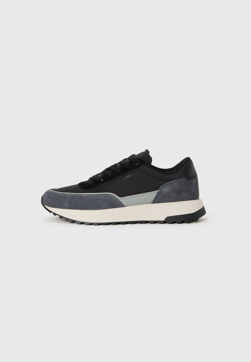 Veterschoenen met een mix van zwarte stof, grijze suède accenten en een stevige witte middenzool met een zwart rubberen loopvlak.