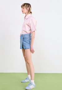 Ljusrosa kortärmad skjorta, åtsittande denimshorts och blåa träningsskor med vita ränder. Slätt tyg och rena linjer.