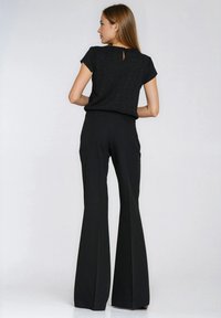 Czarny top z krótkim rękawem z detalem w postaci wycięcia na plecach, zestawiony z czarnymi, rozszerzanymi spodniami. Materiał wydaje się gładki, z dopasowanym krojem.