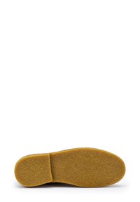 Suela de zapato de ante marrón con una superficie superior texturizada y difusa. La suela exterior es de un material amarillo sólido y duradero con una ligera curvatura.