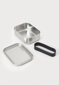 Prostokątne pudełko na lunch ze stali nierdzewnej, z płaską pokrywką i czarnym silikonowym paskiem. Posiada gładką metalową powierzchnię oraz zaokrąglone rogi.