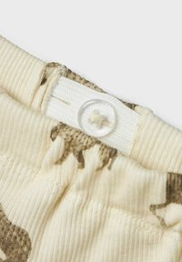 Crème kleurige stof met een ribbeltextuur, met een bruin dierenpatroon en een witte klittenbandsluiting met een doorzichtige knop.