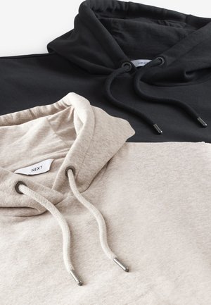 Dva mikiny s kapucí, jedna černá a jedna světle béžová, s šňůrkami a kovovými doplňky. Měkká textura látky, neformální design.